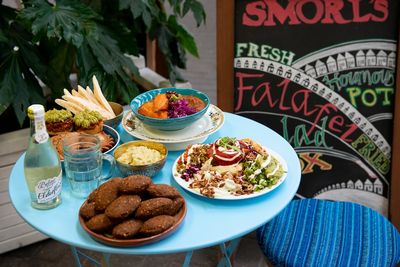 A dish of falafal with plates of salad and homous on a blue table,