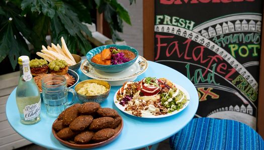 A dish of falafal with plates of salad and homous on a blue table,