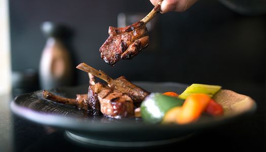 Chargrilled skewered meat with mixed Mediterranean vegetables served on a black dish.
