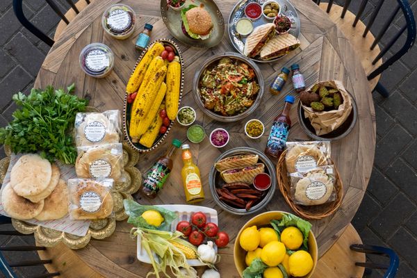 table laid out with colorful food including corns,lemons, hummus, pitta bread, garlic