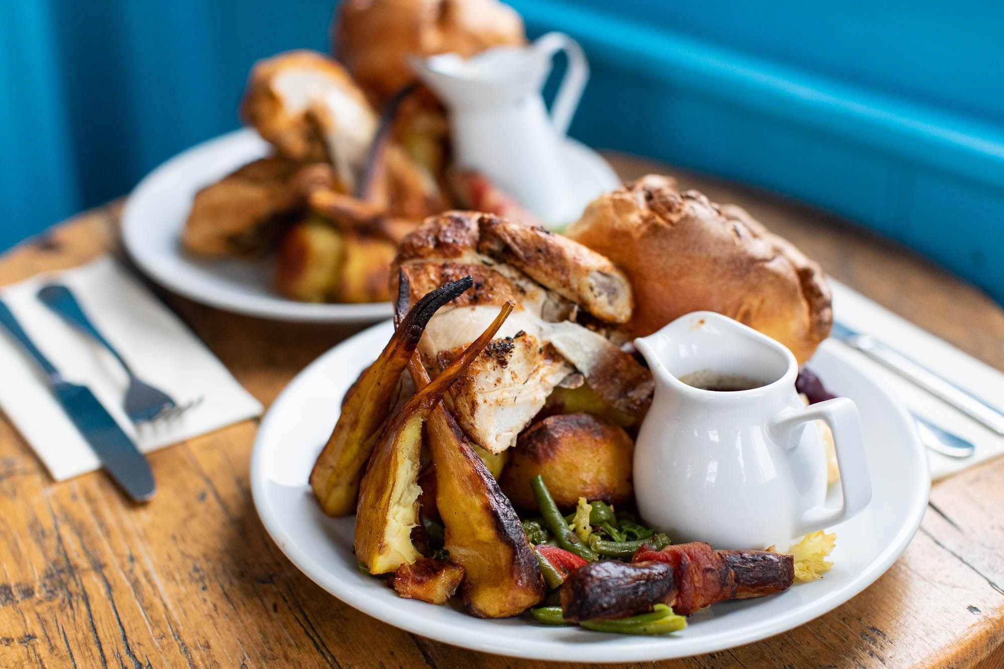 Two award winning Sunday roasts at Haus on the Hill, stacked high with Yorkshire pudding and parsnips and jugs of gravy on a worn wooden table 