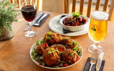 two delicious looking Caribbean dishes served with glass of red and pint on the brown table.