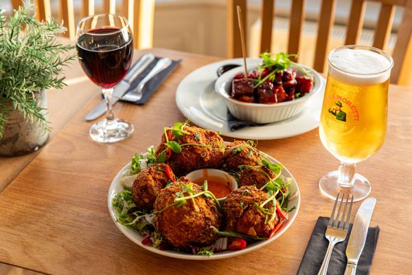 two delicious looking Caribbean dishes served with glass of red and pint on the brown table.