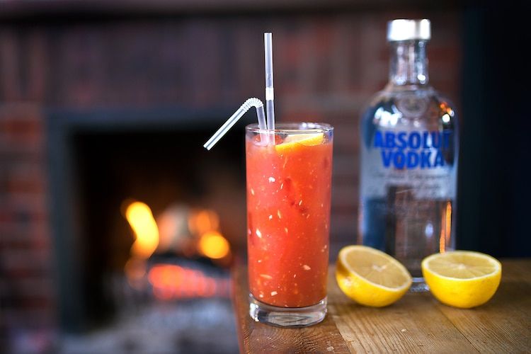 Bloody Mary with straws next to a fresh lemon cut open and a bottle of Absolut Vodka.