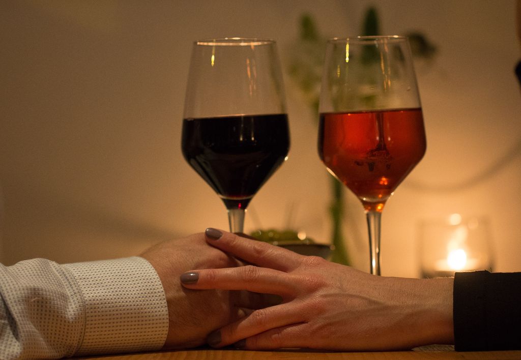 Valentine's Day Brighton in Brighton. Pictured, a romantic couple holding hands with a rose and red wine in hand. Candlelit setting and low light.