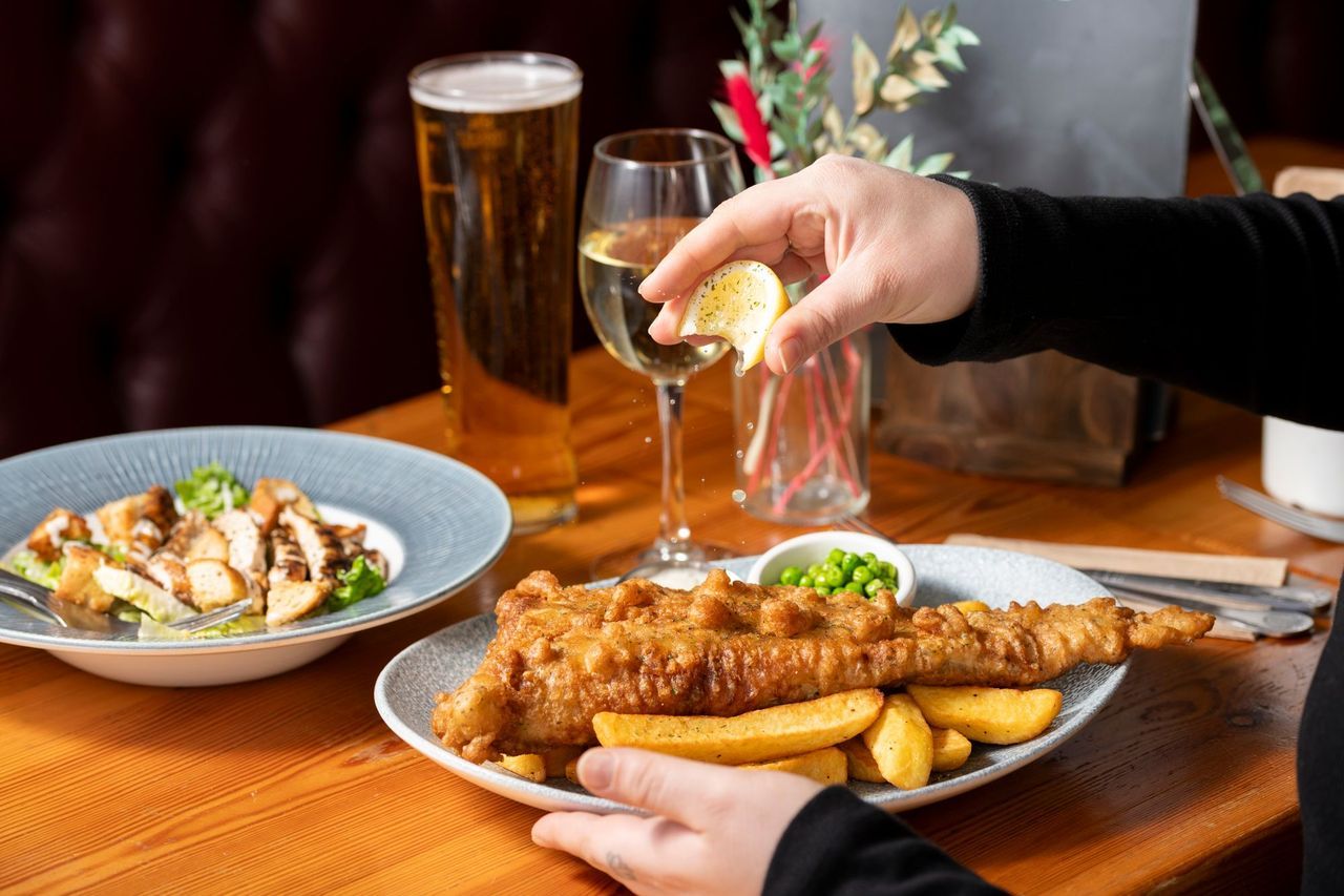 a hand squeezing lemon on big fried fish served with lots of chips at The Dorset pub