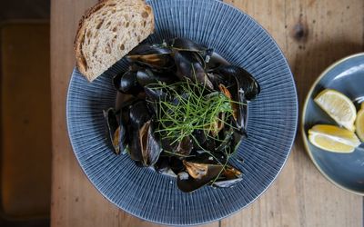 A bowl of mussels in a garlic sauce with crusty bread, fresh herbs and lemon