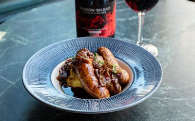 bangers and mash served in the blue plate with glass of red wine on the dark blue marble table