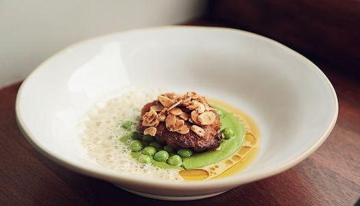 A large deep dish with a creamy pea puree topped with a piece of red meat and toasted flaked almonds
