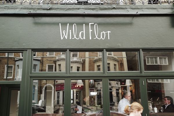Outside of Wild Flor during the daytime. Photography of the front entrance and windows with green paintwork.