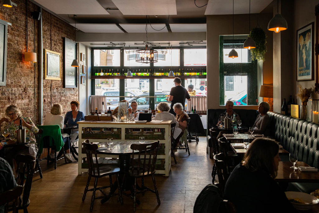Interior photograph of a restaurant with people dining and the floor to ceiling windows letting in natural light.