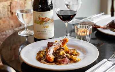 Ellen Richardson – Restaurants Brighton – Wild Flor 19.9.25-34 A white ceramic plate with a meat dish and a tea light in the background with a glass and bottle of red wine.