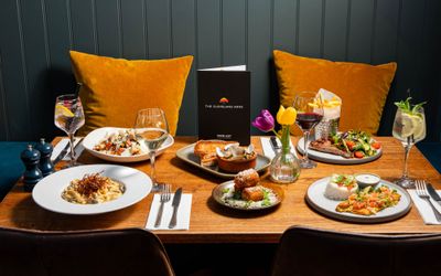 side shot of the brown wooden table laid out with the four main and two side dishes, served with glasses of wine at The Cleveland Arms in Brighton.
