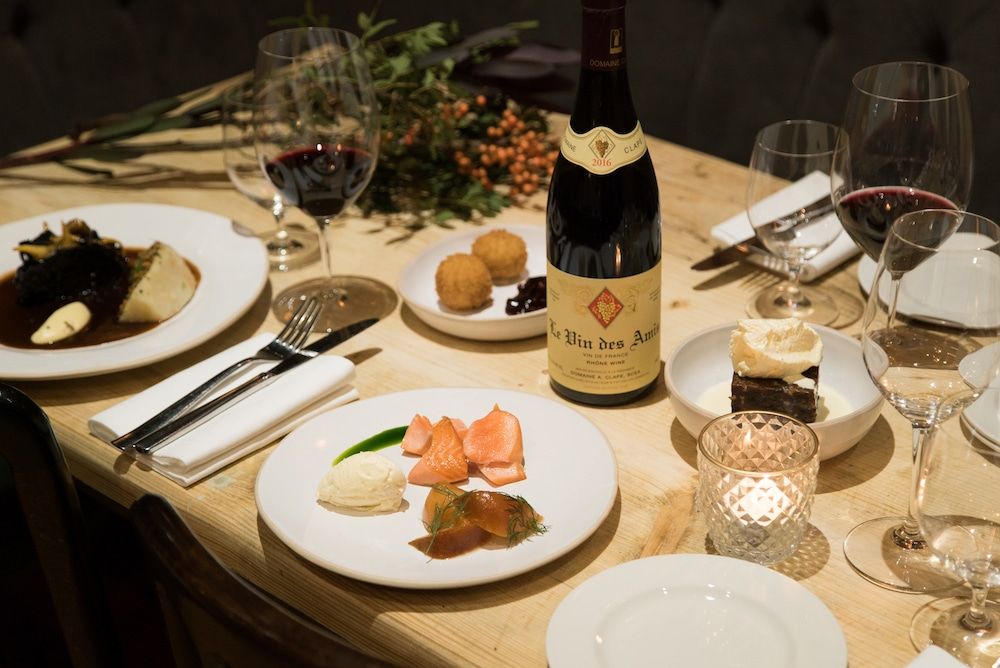 Candlelit tablescape with plates of food, a bottle of red wine and foliage for decoration.