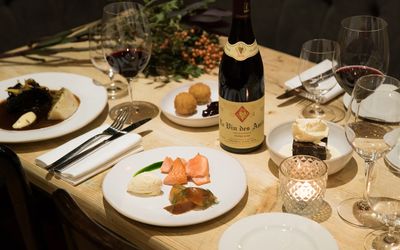 Candlelit tablescape with plates of food, a bottle of red wine and foliage for decoration.