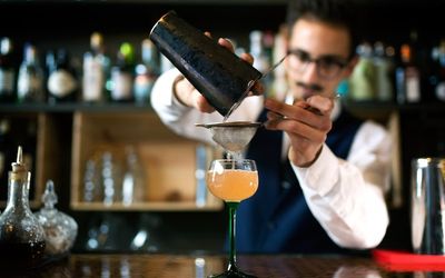 Bar man pouring a bright orange cocktail