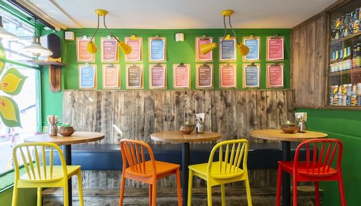 Interior of the Curry Leaf Cafe, Brighton. Colourful chairs and wooden table. A place to enjoy set menus in Brighton, southern indian cuisine.