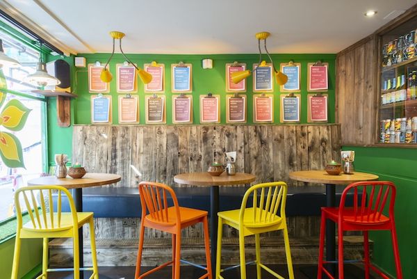 Interior of the Curry Leaf Cafe, Brighton. Colourful chairs and wooden table. A place to enjoy set menus in Brighton, southern indian cuisine.