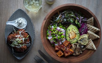A colourful Buddha bowl with avocado and tofu along with a side of cauliflower wings