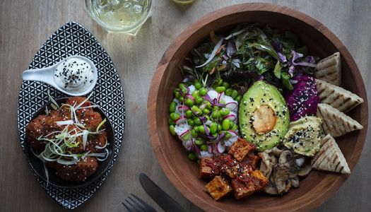 A colourful Buddha bowl with avocado and tofu along with a side of cauliflower wings