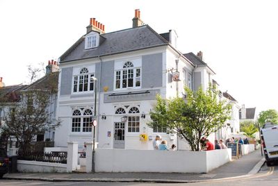 Exterior photograph of the grey pub building on a sunny day with outside seating.