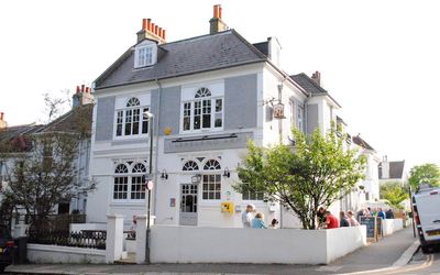 Exterior photograph of the grey pub building on a sunny day with outside seating.