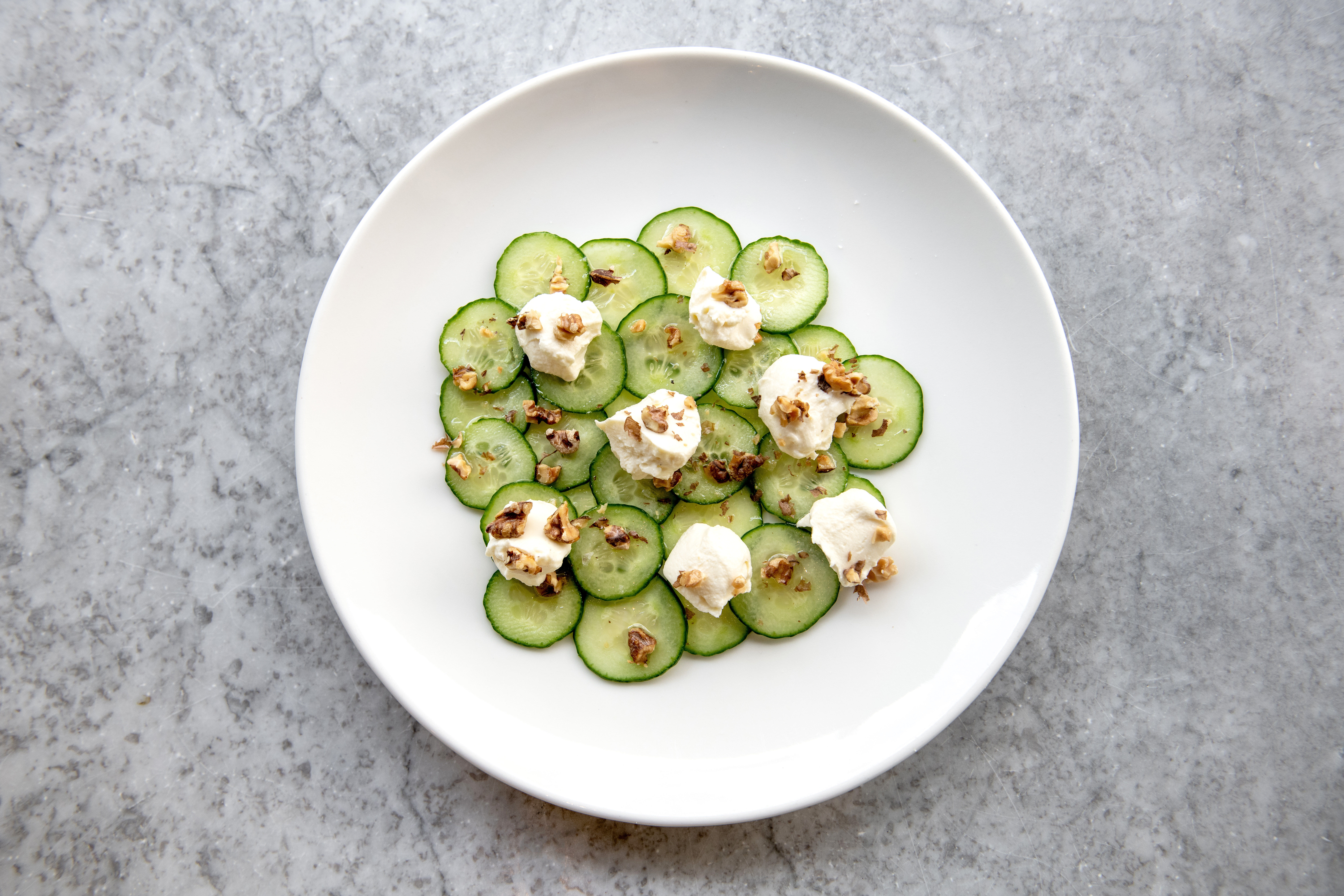 over head shot of the cucumber dish served on white round plate on the grey table