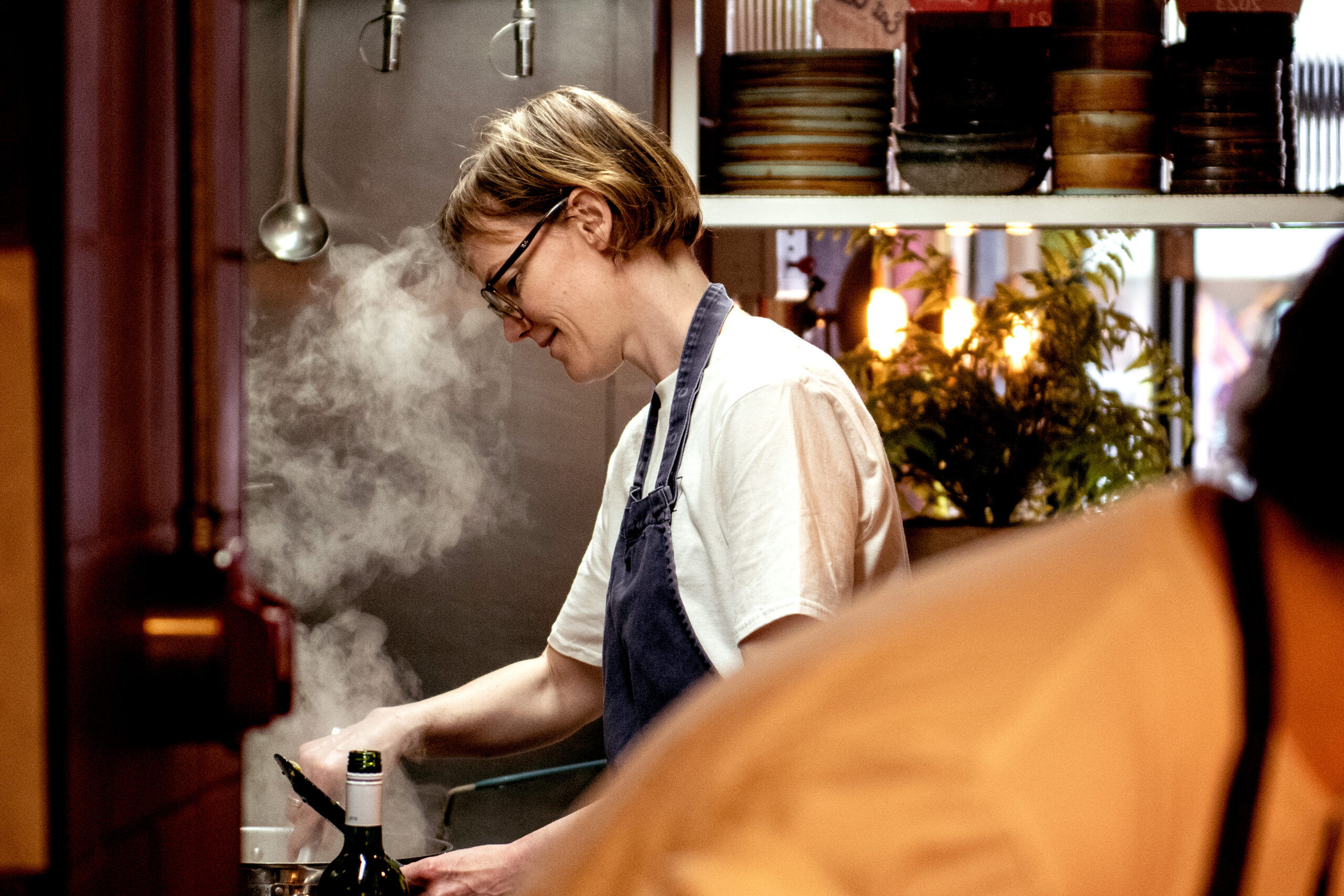 Holly, chef at work over a steaming pan with another chef in the foreground