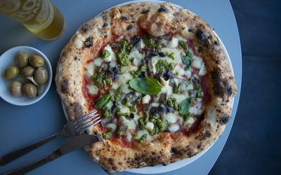 Pizza with pesto, a side of olives and bottle of beer