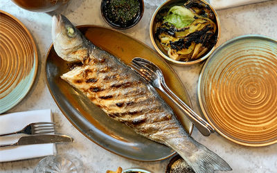 Whole grilled fish on a plate with sides and cutlery