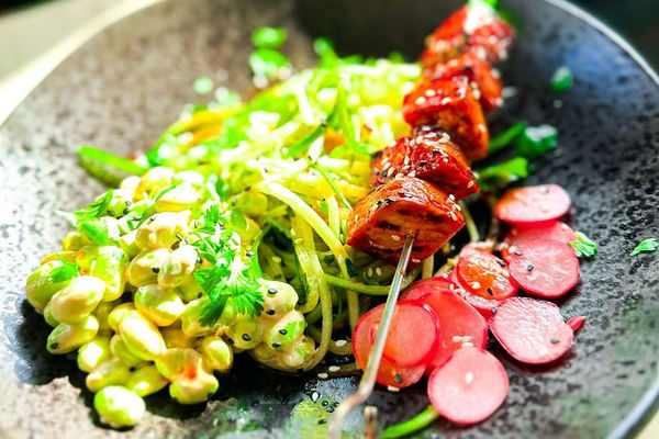 A colourful bowl of ingredients included sliced radishes and a tofu skewer.