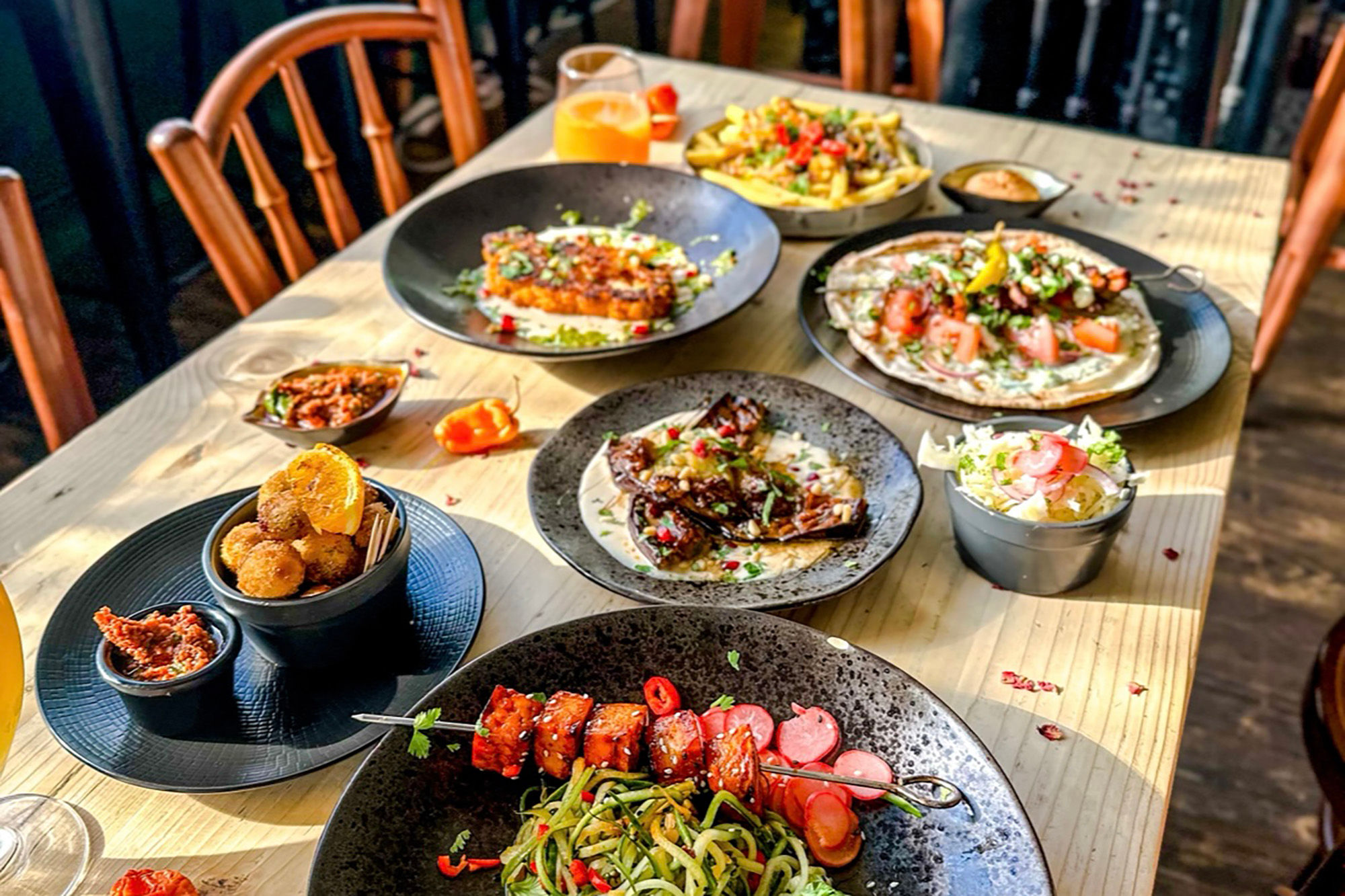 A wooden table with a variety of bowls and plates of colourful vegan food.