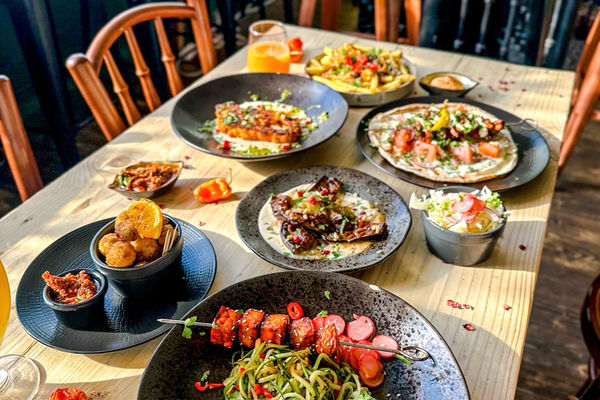 A wooden table with a variety of bowls and plates of colourful vegan food.