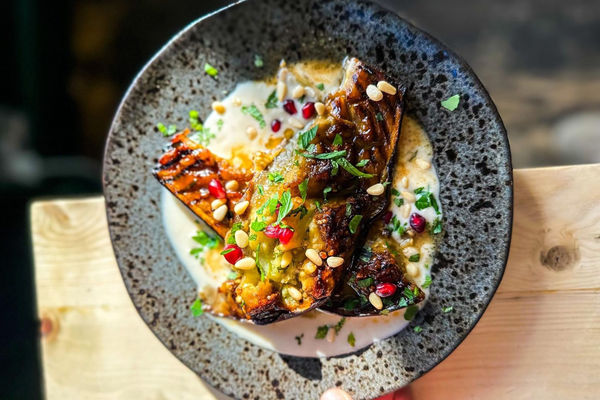 An aubergine dish with pomegranates and fresh chopped herbs captured in natural light on a sunny day.