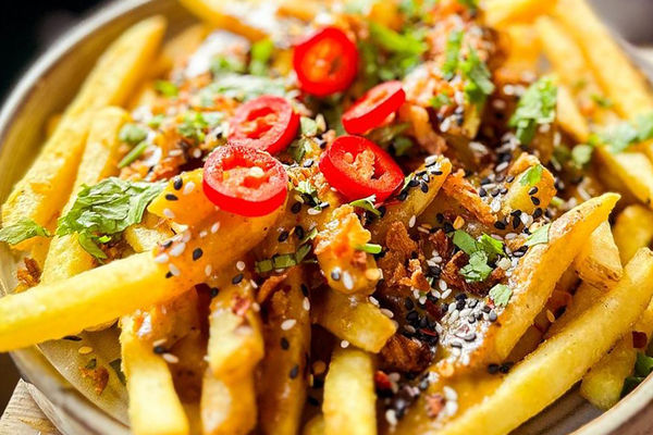A close up photo of loaded fries garnished with sliced red chillies and chopped herbs.