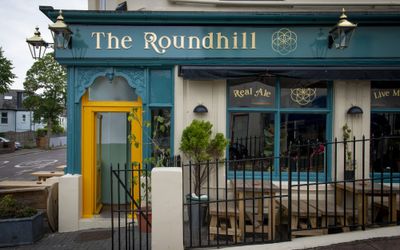 Exterior of The Roundhill with teal and mustard paintwork and outside tables.