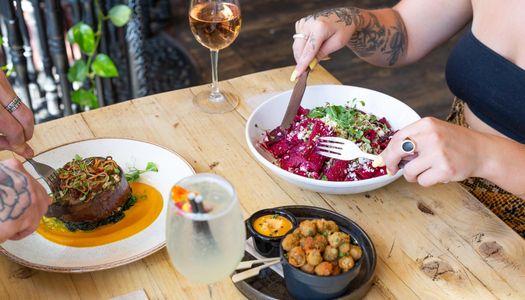 two people by the table, both eating vegan dishes served with glasses of wine