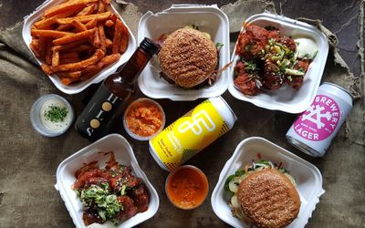 Takeaway boxes of sweet potato fries, cauliflower wins, burgers, dipping sauces and cans of beer.