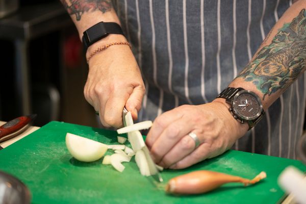 close up photo of the tattoed hands cutting onion with the knife on the green board