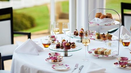 High tea served on a table dressed with a crisp white table cloth. Serving a variety of French patisseries, cake and champagne.