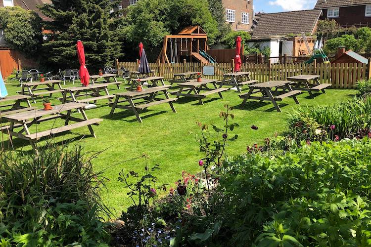 Traditional kitchen garden with a children’s play area. Wooden benches lined up with parasols and plant pots.