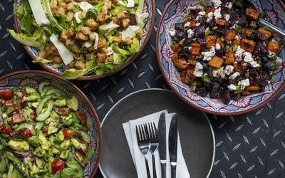 Bowls of salads including a roasted vegetable salad, an avocado salad and a caesar salad.