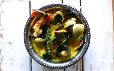 A metal bowl of seafood curry with prawns and mussels