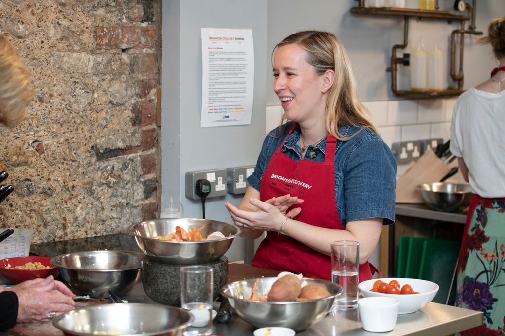 blonde woman in the blue shirt smiling by her table while cooking