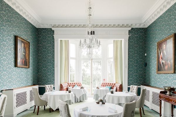 Restaurant Interlude. Showing inside of restaurant. with round tables with white linen, very much a fine dining setting. The room has very tall windows, a chandelier and blue wall paper. A Michelin star restaurant in Sussex, a drive away from Brighton