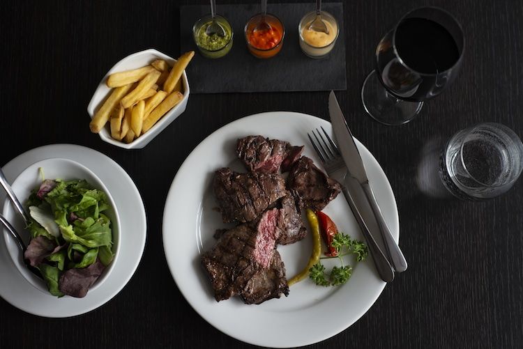 Steak and chips with three dipping sauces. Served on a dark surface with a glass of red wine.