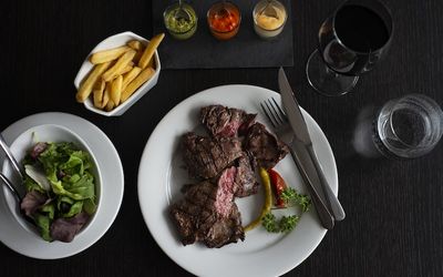 Steak and chips with three dipping sauces. Served on a dark surface with a glass of red wine.