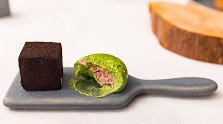 A filled green sponge and chocolate square cake served on a mini grey chopping board