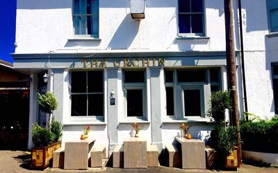 Exterior photography of the white painted pub building with the sun shining, plants and outside seating.