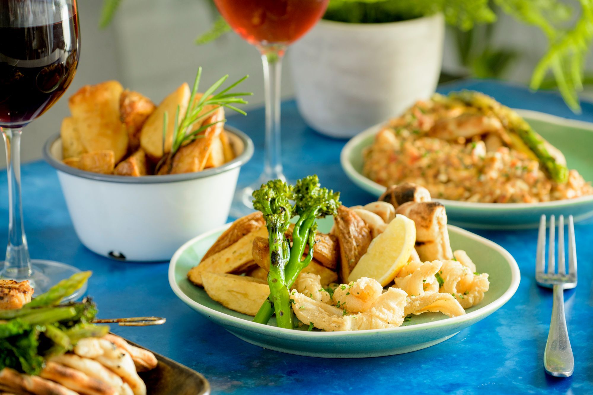 side shot of the couple of greek dishes served in white plates and with glasses of red wine